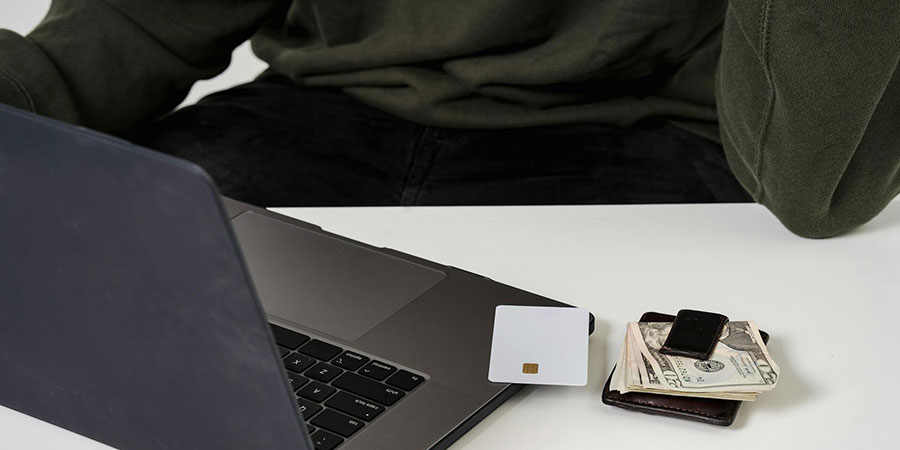 a person using a laptop and a credit card beside a wallet full of US dollar bills